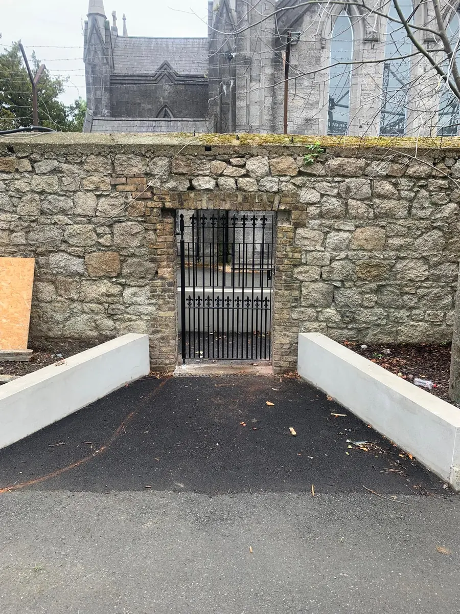 A wrought iron style pedestrian gate in black steel with finials and dog bars, made to fit an opening in an old stone wall