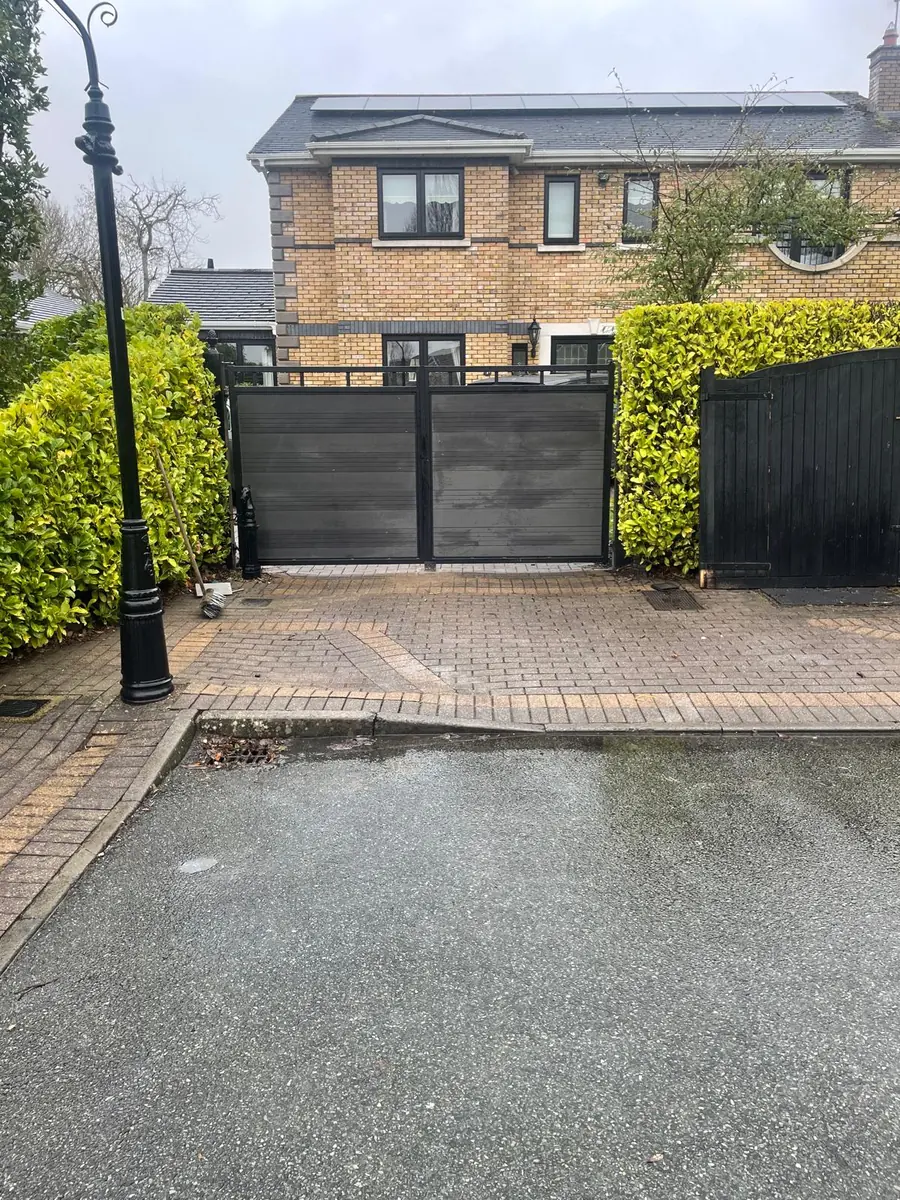 A pair of made to measure driveway gates with a black steel frame and grey composite board infill between hedges at a brick house