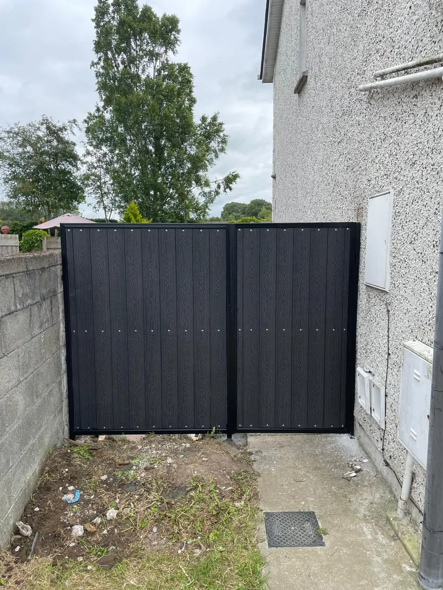 A double metal side gate with a black steel frame and black composite infill closing a wide passage beside a house