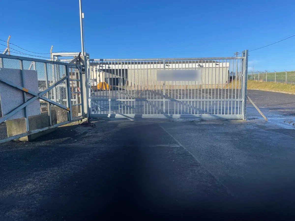 A wide galvanised steel sliding gate with upright bars across the entrance to a commercial yard