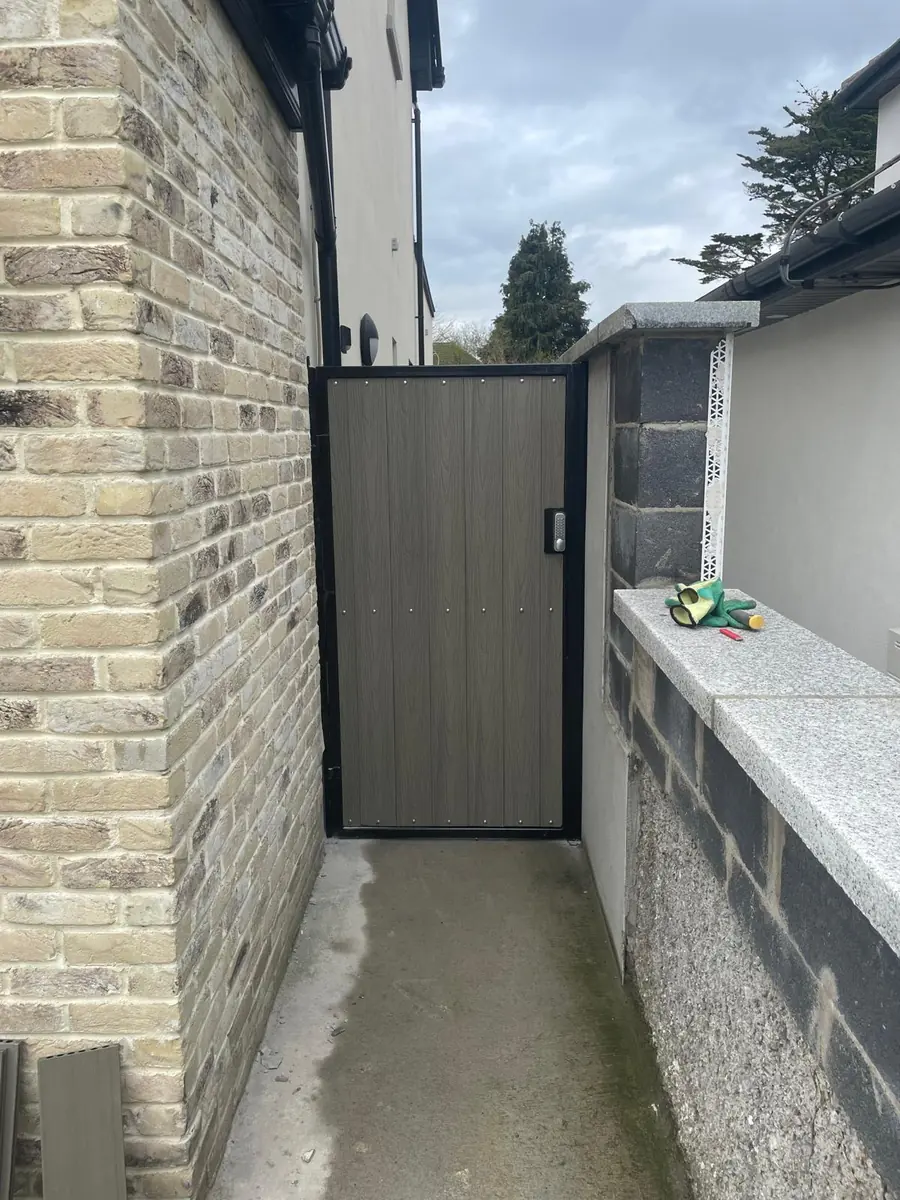 A made to measure metal side gate with a black steel frame and grey composite board infill fitted between a brick house and a boundary wall