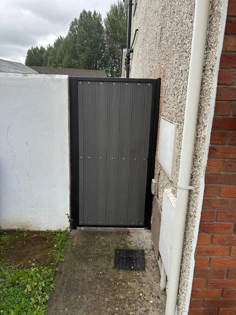 A steel framed side gate with grey composite infill fitted between a house wall and a rendered boundary wall