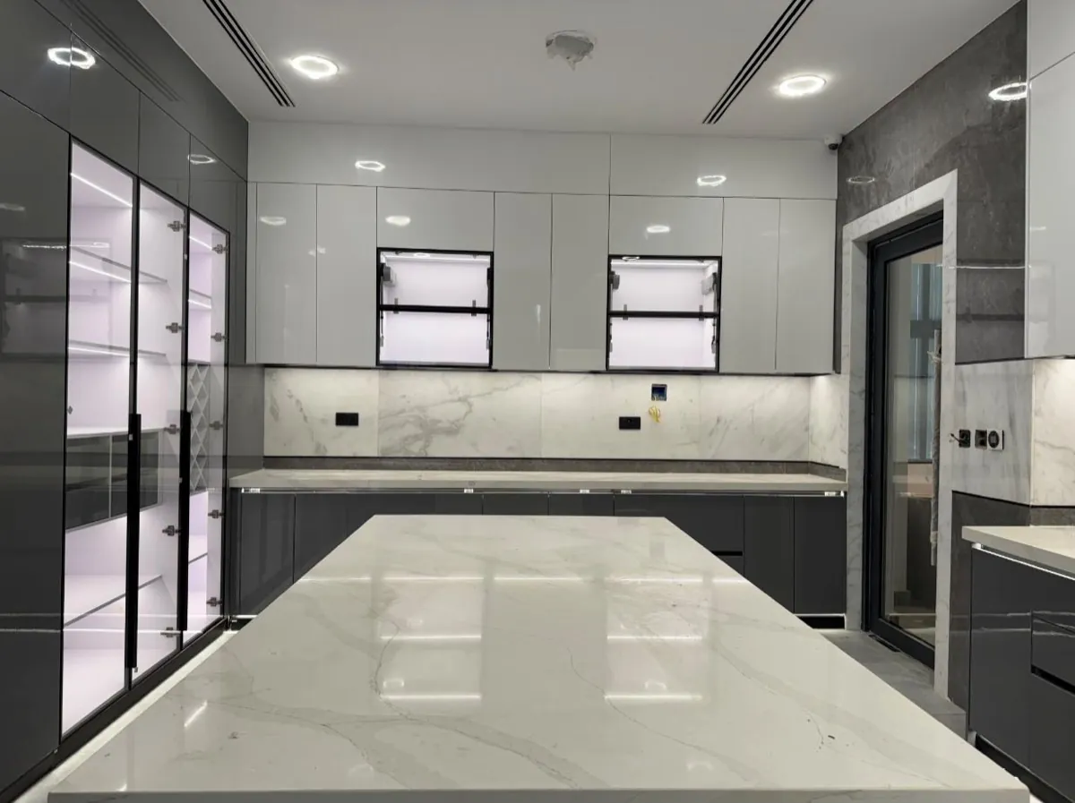 A large custom kitchen in grey and white gloss with a marble worktop island and backlit display cabinets