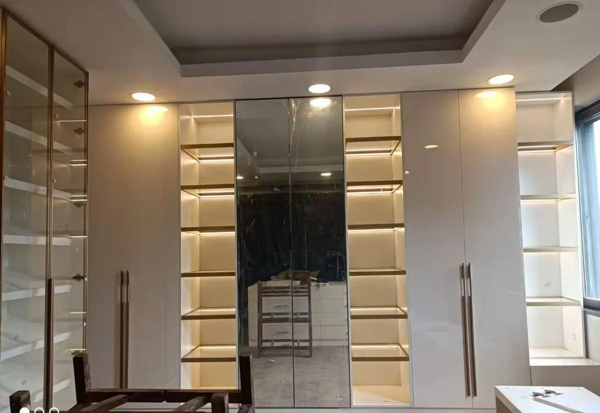A walk in wardrobe with lit shelving, hanging rails, drawers and glazed sliding doors